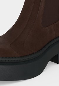 Bottine en daim marron foncé avec panneau latéral élastique et épaisse semelle plateforme noire avec talon bloc.