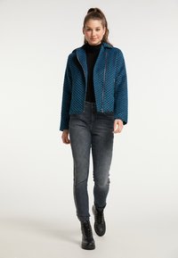 Niebieska i czarna kurtka w wzory z zamkiem z przodu, połączona z szarymi dżinsami z bocznymi ozdobami i czarnymi sznurowanymi butami.