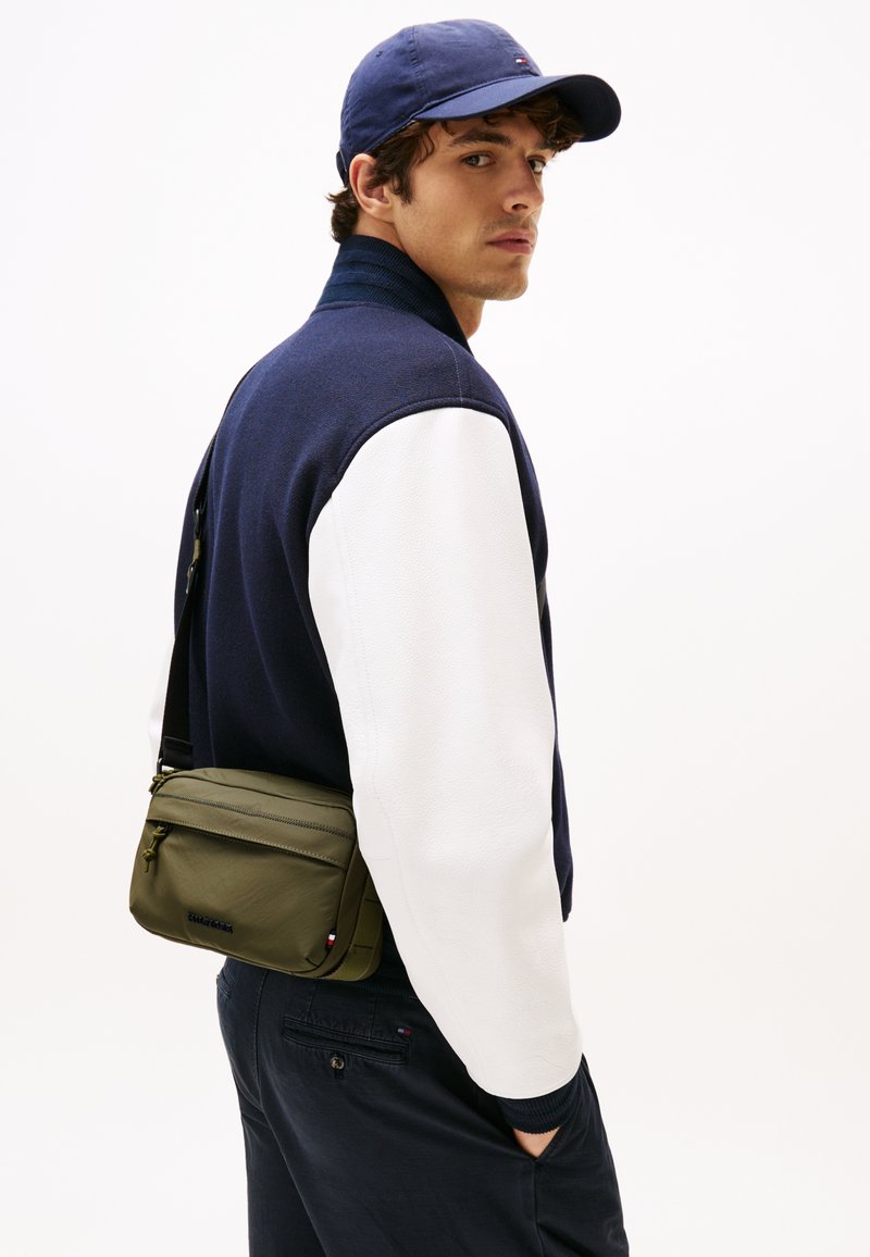 Navy and white color-blocked jacket with a textured upper fabric and smooth leather sleeves, paired with a small olive green crossbody bag.