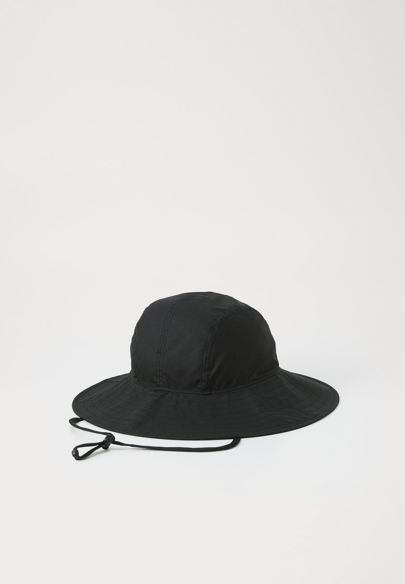 Musthave musta müts lai äärega, mis on valmistatud kergest kangast. Omab õmmeldud õmblusi ja reguleeritavat köit lõua all.
