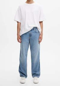 Bílé bavlněné tričko s nízkými rameny, v kombinaci s volnými světle modrými džíny a bílými teniskami. Jednoduchý, ležérn�í design.