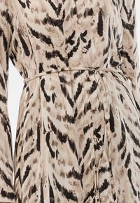 Φόρεμα με κουμπιά με μπεζ και μαύρο animal print. Το ύφασμα είναι λείο με ζώνη στη μέση και μακριά μανίκια, επιδεικνύοντας έναν κλασικό σχεδιασμό.