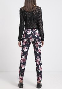 Kalhoty s květinovým vzorem v tmavě námořnické barvě, s přiléhavým střihem a růžovými a bílými květy, doplněné černým krajkovým topem a černými botami.