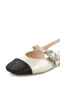 Ballerine di colore crema con punta tessuta nera, cinturino regolabile e una fibbia decorativa con embellissements trasparenti.