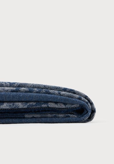 Tissu à motifs bleu et gris plié, montré en gros plan sur une surface blanche unie.