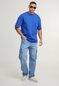 Blå bomulds t-shirt med korte ærmer, parret med lyseblå cargo jeans med overdimensionerede sidelommer og hvide sneakers.