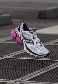 Baltas sportinis batų modelis su rožiniais ir juodais akcentais, pasižymintis tinklelio viršumi, paminkštintu apykakliu ir išraiškingu amortizuojančiu padu.