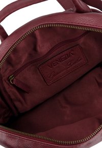 Burgundy leather handbag interior with a smooth, textured finish, featuring a small zip pocket and a fabric lining with stitching details.