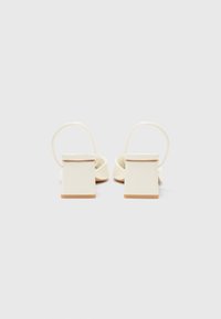 White heeled sandals with a square heel and slender ankle straps. Smooth texture, minimalistic design, and understated color palette.