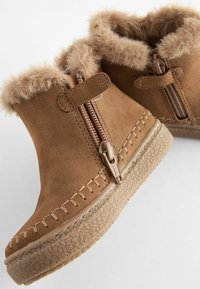 Stivaletti in suede beige con bordino in pelliccia sintetica, dotati di doppie cerniere laterali e suole in gomma texturizzata. Dettagli cuciti a mano sulla parte superiore.