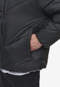 Jachetă puff black cu quilt-uri în formă de diamant, fermoar în față și buzunare laterale. Material moale și lucios, cu o croială relaxată.
