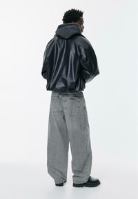 Schwarzer, glänzender, übergroßer Hoodie mit grauer Kapuze, kombiniert mit locker sitzenden grauen Jeans und schwarzen klobigen Stiefeln. Minimalistisches Design, keine sichtbaren Logos.