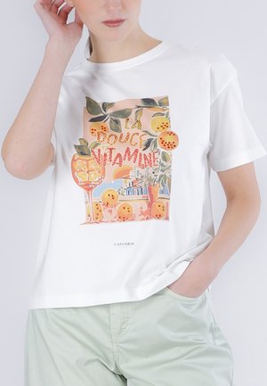 Kobieta w białej koszulce z kolorowym nadrukiem pomarańczy, liści, szklanki z lodem oraz napisem "La Douce Vitamine".