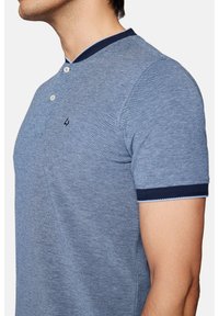 Koszulka polo z krótkim rękawem w niebieskim melanżowym kolorze, z granatowym kołnierzykiem i wykończeniami rękawów, z zapięciem na dwa guziki oraz subtelnym logo na klatce piersiowej.