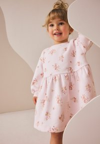Robe florale rose avec manches longues, taille froncée et tissu doux. Présente de petites fleurs pastel et des poignets côtelés.