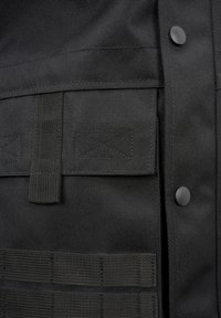 Tessuto tattico nero con superficie testurizzata, dotato di una patch in velcro, fascia elastica e chiusura a bottone. Include una rete a griglia per il fissaggio.