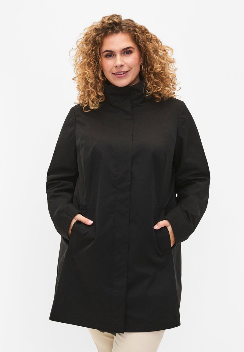 Black waterproof coat with high collar, two front pockets, and a straight cut. Smooth texture and minimalistic design with no visible hardware.