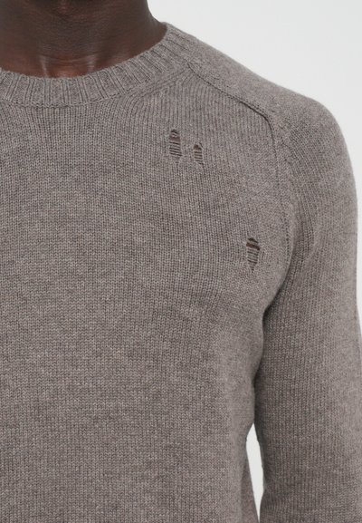 Pull en laine de couleur marron clair, avec un col rond et de légères zones effilochées sur le devant. Motif de tricot texturé sur l'ensemble.