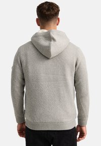 Sudadera de punto gris con un acabado texturizado, que cuenta con una capucha forrada y puños acanalados. El diseño incluye un patrón sutil y una silueta ajustada.