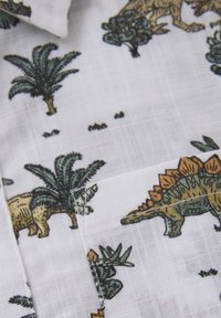 Lichtgewicht, witte stof met een kleurrijke print van dinosaurussen en palmbomen. Opvallende details zijn de gedetailleerde texturen en variatie in kleuren.