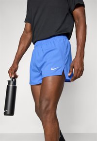 Nike Sportshorts in Blau mit perforierter Struktur, elastischem Bund und seitlichen Schlitzen. Eine schwarze Wasserflasche wird in der rechten Hand gehalten.
