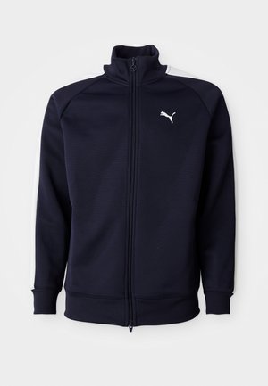 Mørkeblå hættejakke med lynlås, høj krave, ribbede manchetter og kant. Har hvide sidestriber og et lille hvidt Puma-logo på brystet.