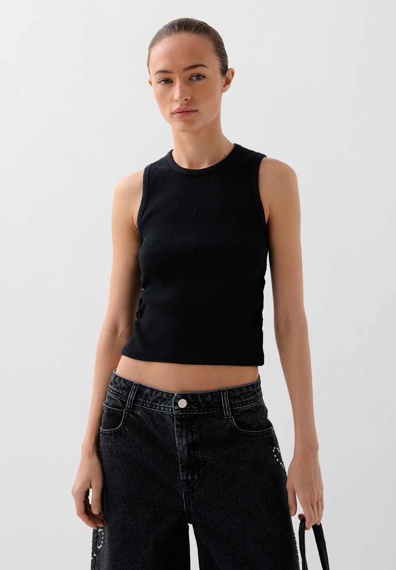 Top sotto con coste nere dal design aderente. Abbinato a jeans in denim neri a vita alta con dettagli in perline e chiusura a bottone.