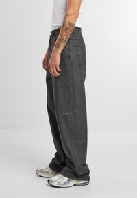 Baggy svarte denimjeans, teksturert stoff, høy midje, front- og baklommer, broderte detaljer, brukt med skinnende sølv sneakers.