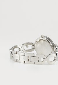 Montre-bracelet en métal argenté avec un bracelet en maillons et un cadran rond. Présente des maillons polis et un fermoir de marque avec des détails gravés.