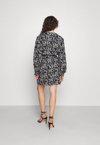 Robe à manches courtes, noire et blanche avec un motif, cintrée à la taille et ourlet inférieur évasé. Dotée d'un col rond et de manches longues.