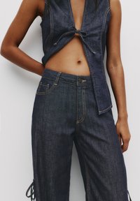 Denim sleeveless top med detaljerad knut framtill, kombinerad med högmidjade, vida denimbyxor med kontrasterande sömmar och sidband.