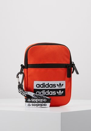 Petit sac bandoulière rectangulaire orange Adidas avec fermeture éclair noire, patchs logo blancs et noirs, et sangle de marque sur surface blanche.