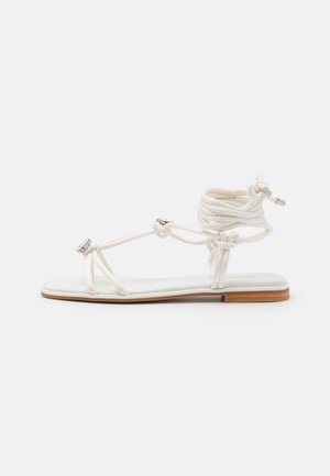 Sandalias planas blancas con un diseño de tiras con nudos, plantilla acolchada y detalle de suela de madera.