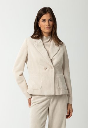 Blazer en velours côtelé beige avec un design double boutonnage, deux poches à l'avant et un col cranté. Tissu texturé avec des rayures verticales.