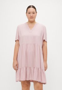 Φόρεμα κοντομάνικο, σε σχήμα V, σε ανοιχτό ροζ, με φουσκωτή φούστα και ραμμένο βολάν στο τελείωμα. Φτιαγμένο από μαλακό, ελαφρύ ύφασμα.