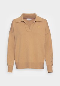 Pull beige en maille avec col en V et col. Dispose de poignets et d'un ourlet côtelés, ainsi que d'un subtil détail monogramme doré sur la poitrine.
