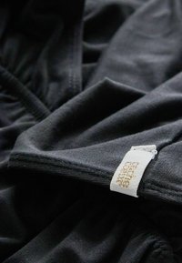 Tissu noir avec une texture lisse et un léger élasticité ; présente une étiquette blanche avec un texte doré cousu dans la couture.