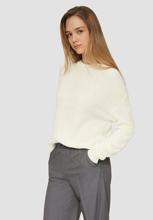 White knitted sweater with a relaxed fit and ribbed cuffs, paired with gray trousers. The sweater features a textured finish and a crew neck.