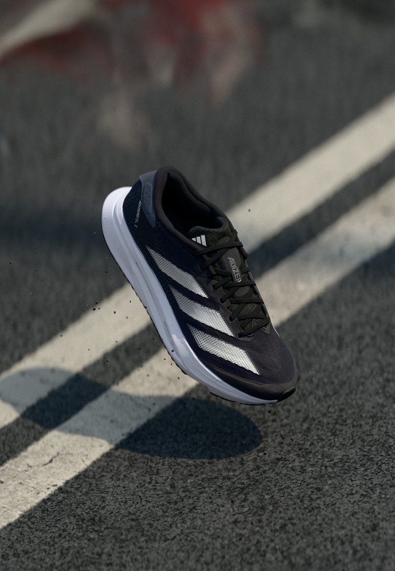 Black athletic shoe with white stripes, sleek design, textured fabric, lightweight construction, and a rounded sole, suspended above a pavement.