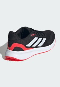 Chaussure de sport noire avec des rayures blanches, empeigne en maille texturée et semelle blanche et rose. Design durable avec un talon rembourré pour le confort.