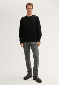 Schwarzer, gerippter Strickpullover kombiniert mit grauen, schmal geschnittenen Hosen und schwarzen Leder-Stiefeletten. Einfaches, modernes Design ohne auffällige Muster.