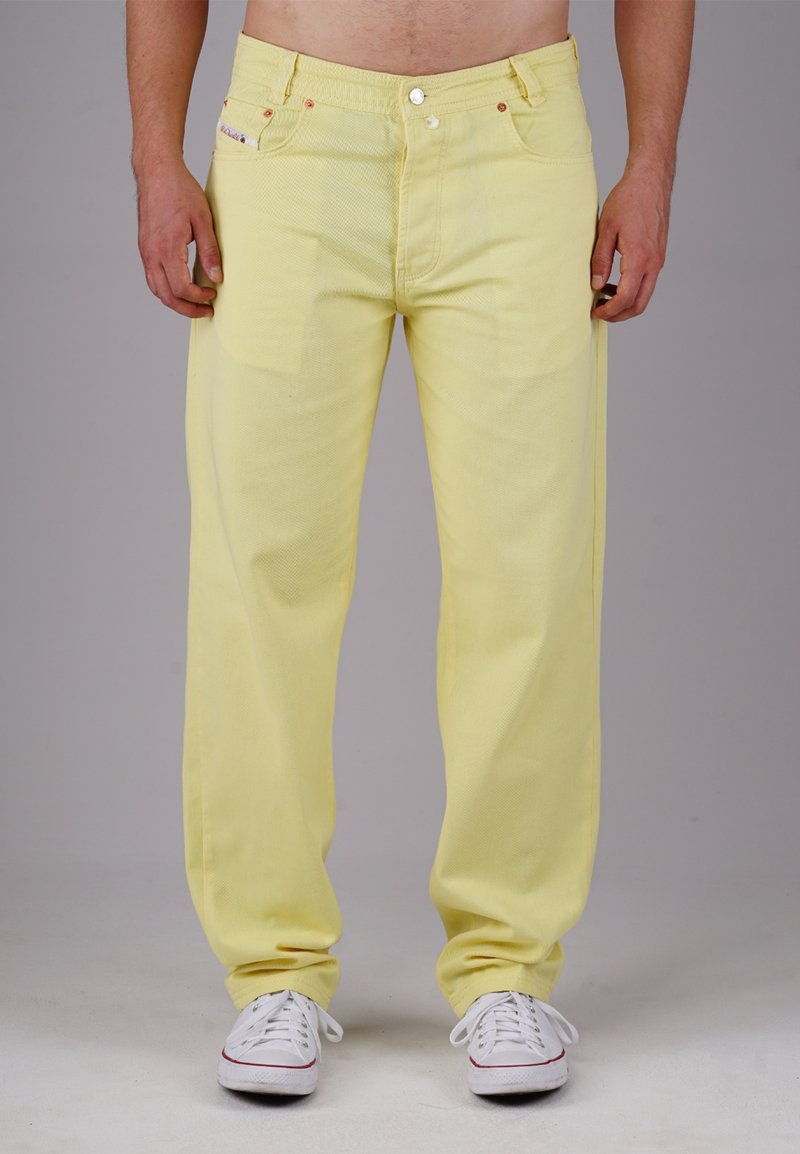 Yellow denim pants with a relaxed fit, featuring five pockets, a zip fly, and metal hardware, worn with white sneakers.