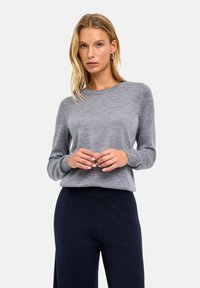 Szary sweter z długim rękawem o miękkiej fakturze, z okrągłym dekoltem i ściągaczami na mankietach, zestawiony z ciemnogranatowymi szerokimi spodniami.