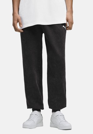 Sorte, løstsiddende sweatpants med en let struktureret overflade og et hvidt Puma-logo på siden, parret med hvide sneakers.
