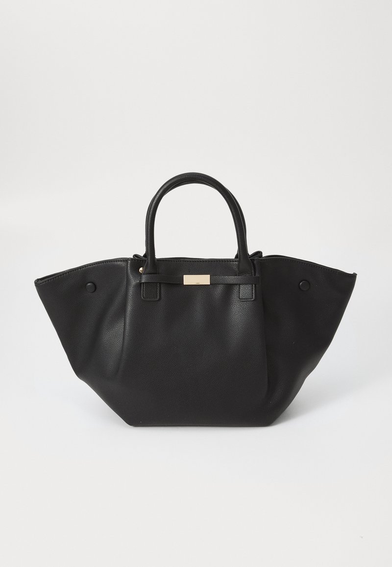 Sac cabas en cuir noir avec des poignées structurées et des côtés larges évasés, avec un petit accent rectangulaire doré sur la sangle avant.