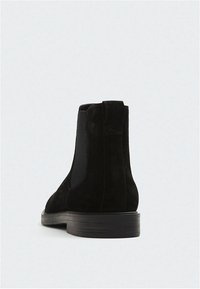 Bottines en daim noir avec des panneaux latéraux élastiques, un bout rond et un petit talon. La semelle est lisse avec une finition mate contrastante.