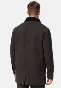 Abrigo de lana marrón oscuro con cuello de sherpa negro, corte recto y mangas largas. Cuenta con una abertura en la espalda para mayor movimiento y un acabado limpio.