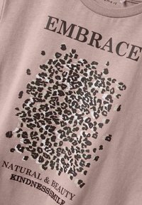 Sweatshirt en coton rose clair avec un graphique imprimé léopard et le texte "ACCUEIL LA BEAUTE NATURELLE & LA GENTILLESSE/SOURIRE" en noir.