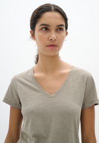 V-hals, kortekous shirt in een lichte khaki kleur, gemaakt van zachte stof met een subtiele textuur en stiksels langs de halslijn.