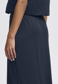 Das navyblaue Kleid hat einen lockeren Schnitt mit einem elastischen Taillengummi, einer glatten Textur und einem weichen Stoff, der elegant fällt.
